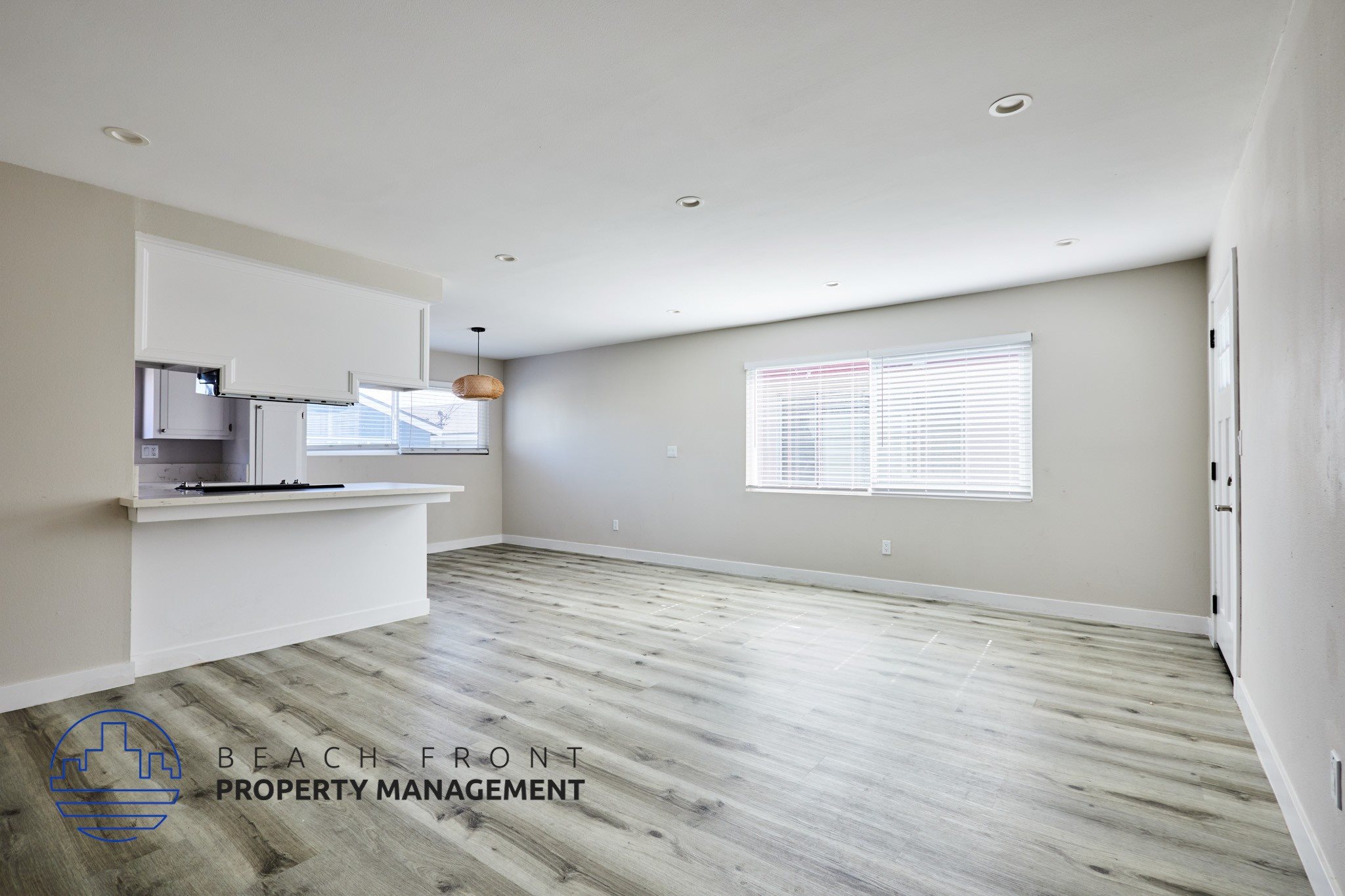 A spacious room with wooden flooring and a window with blinds.
